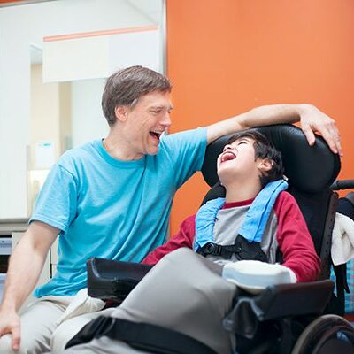 Father laughing with his son in a motorized chair.